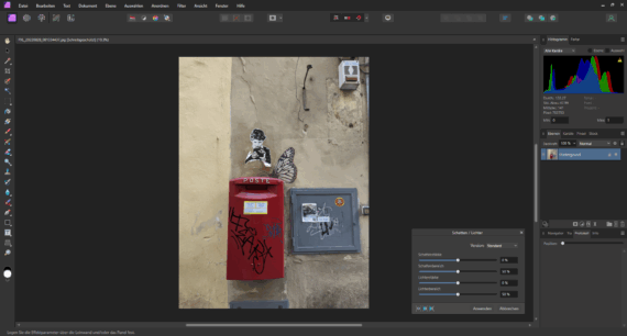 Ein roter Briefkasten mit Graffiti ist an einer beigen Wand angebracht, darunter eine schwarz-weiße Schablone mit einem Jungen und einem großen Schmetterlingsbild. Auch Stromkästen sind an der Wand angebracht. (KI generierte Beschreibung)